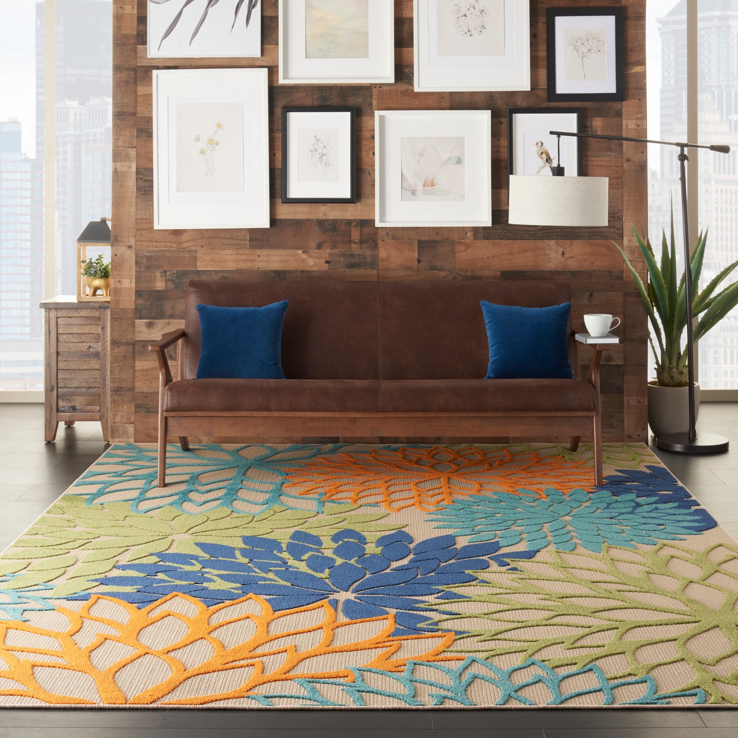 Brown leather sofa with blue cushions in a modern rustic living room; colorful floral area rug and framed art on wood wall.