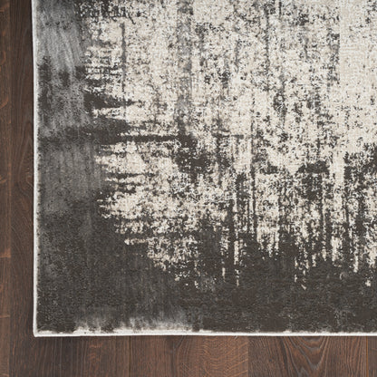 Abstract distressed area rug in charcoal, beige & ivory with light border on dark hardwood floor.