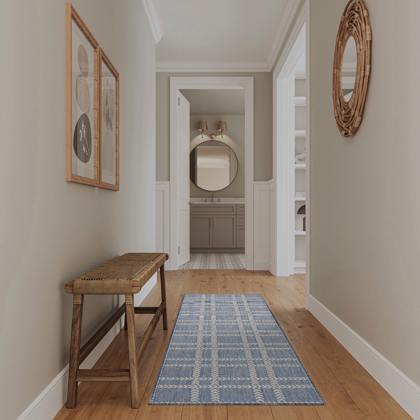 Neutral hallway with blue plaid runner rug, wooden bench, wicker round wall mirror and framed art; opens to a beige bathroom vanity.