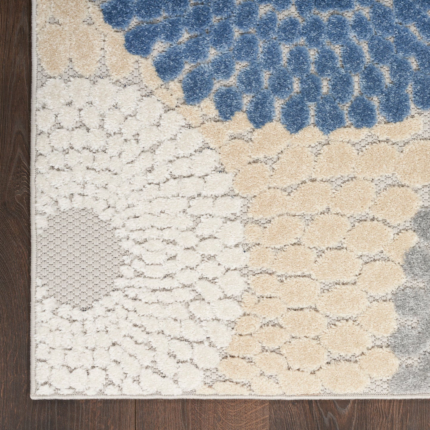 Patchwork tufted rug with blue upper section, cream and beige circular clusters, on dark wood floor.