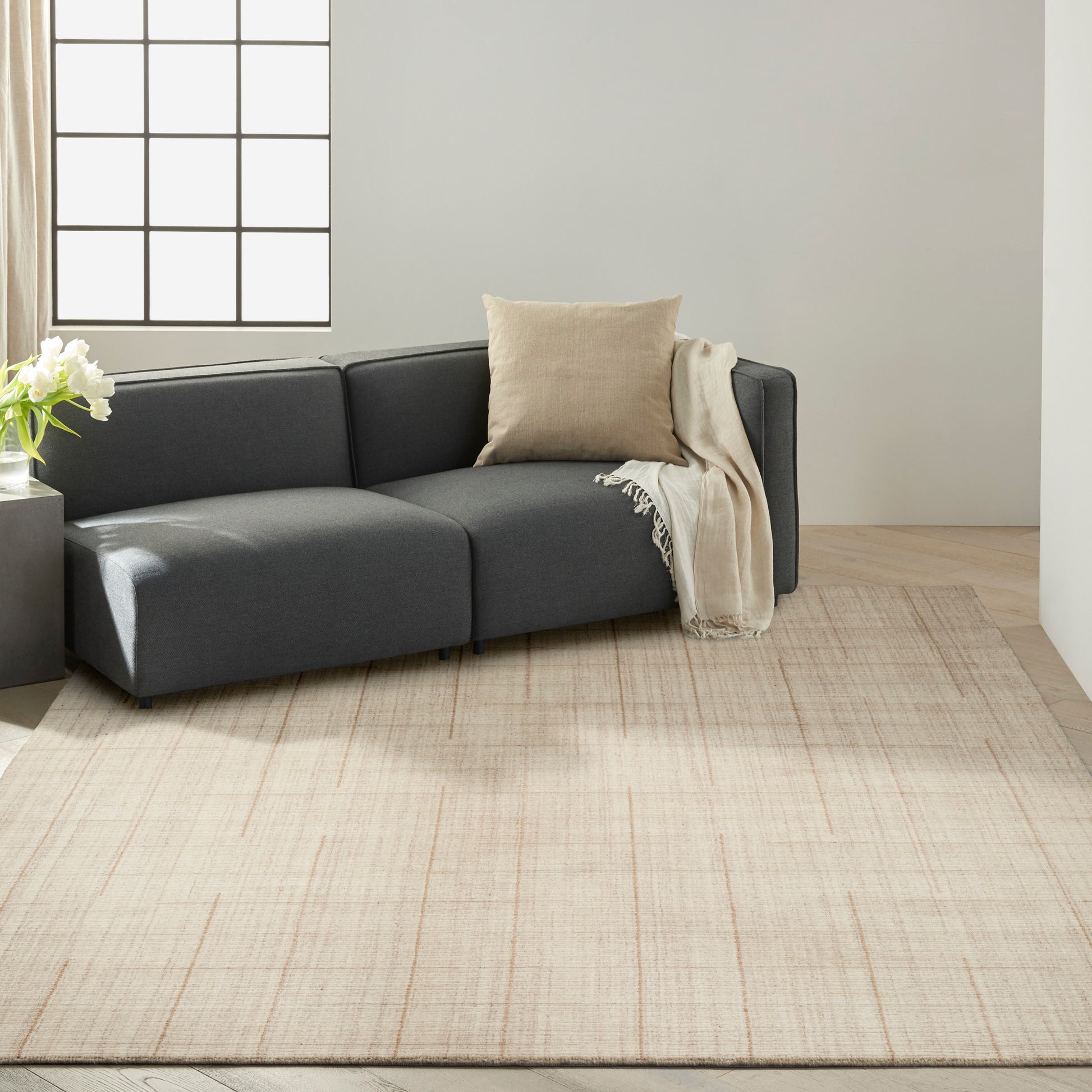 Dark gray sectional with beige throw and cushion on pale rug in bright living room
