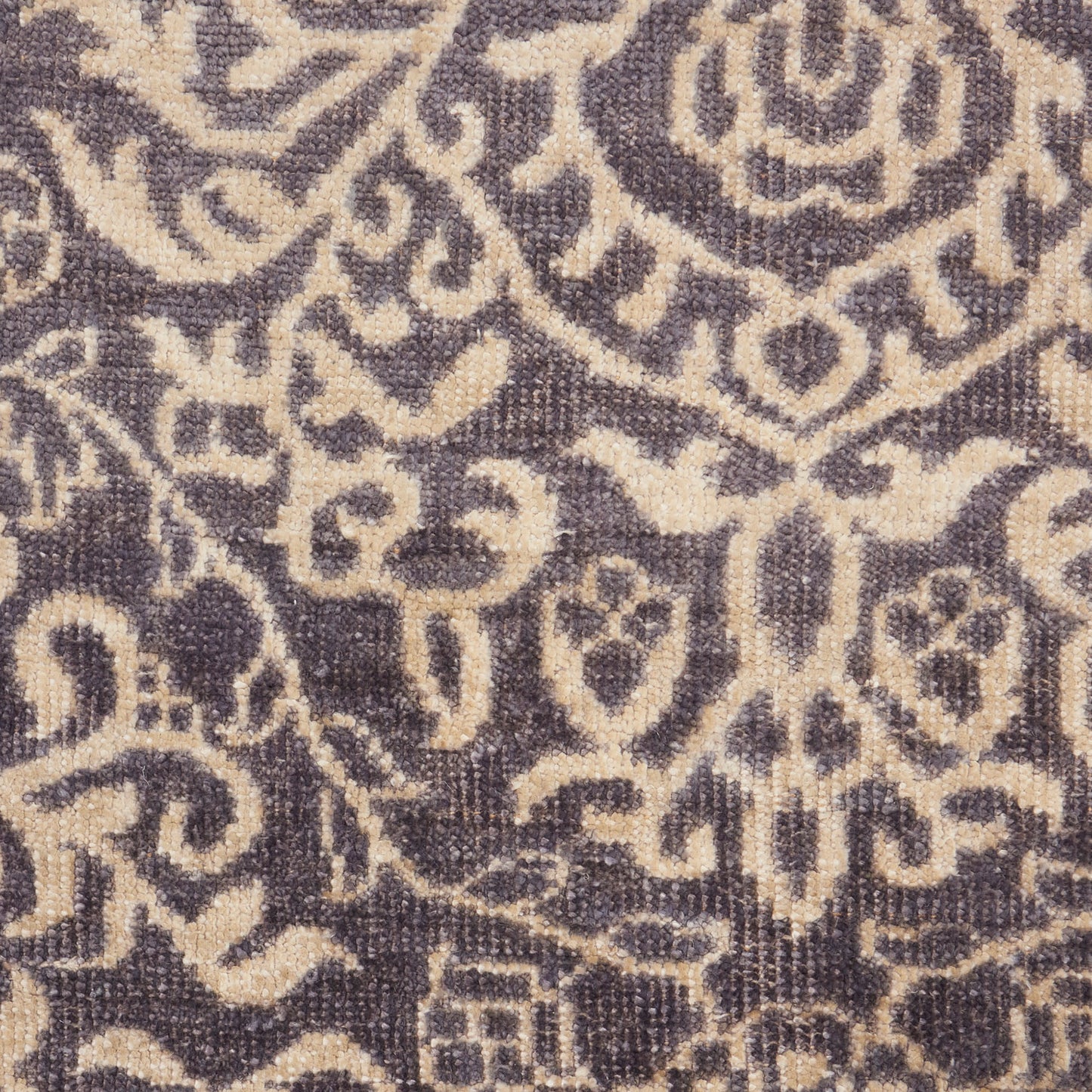 Damask patterned rug in taupe-beige on a deep purple background; ornate curling motifs.