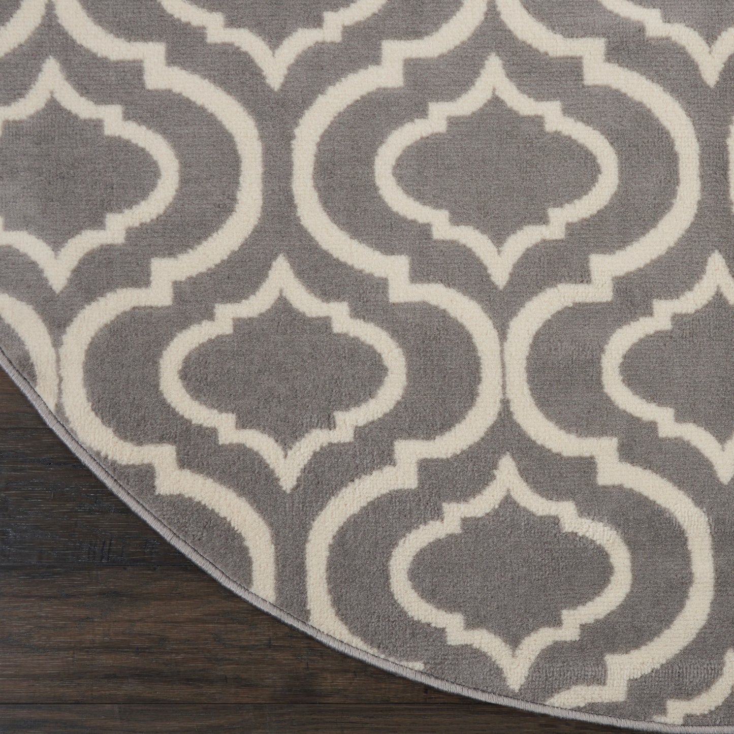 Round grey rug with white arabesque quatrefoil motif on dark wood floor.