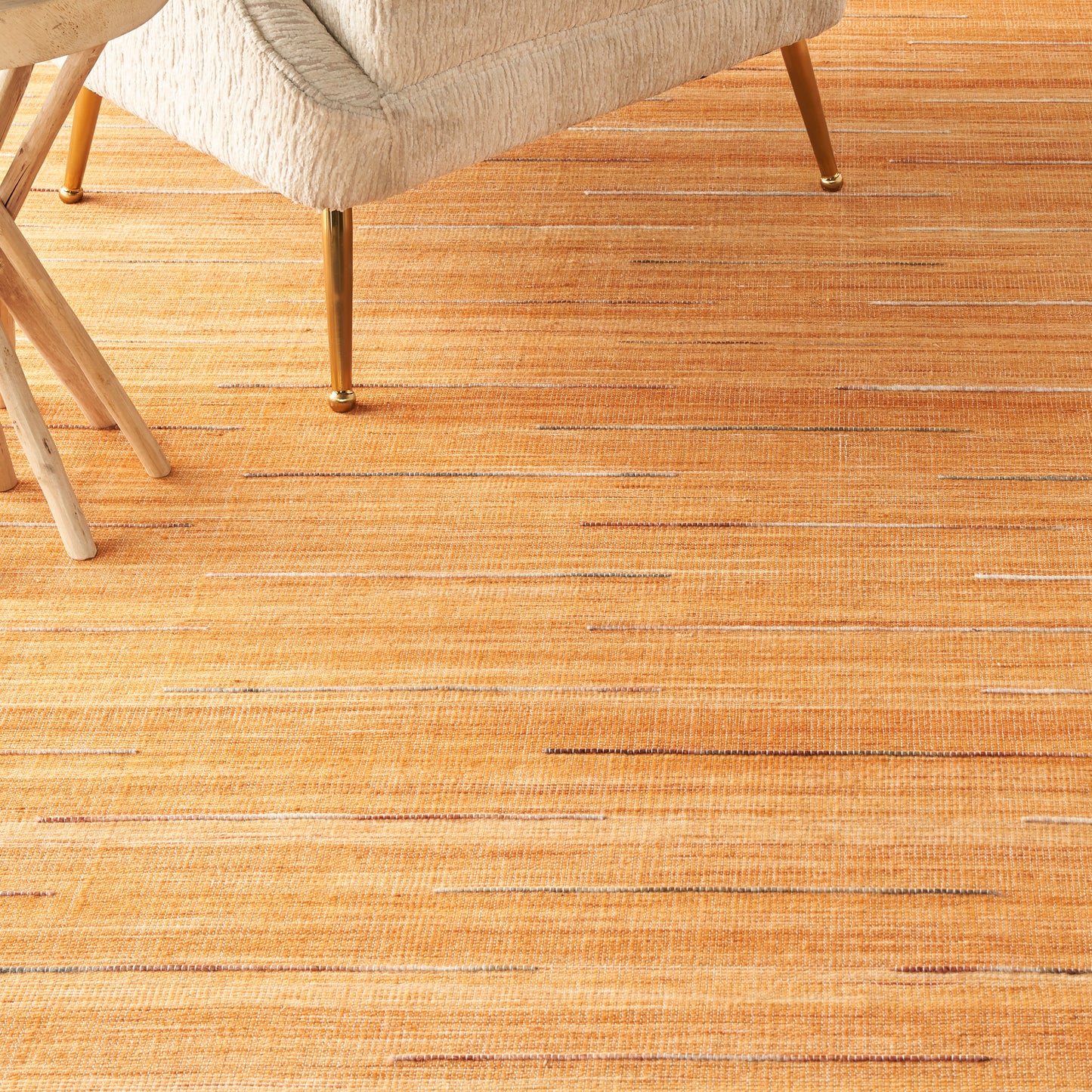 Cream upholstered chair with gold-tone metal legs on an orange striped woven rug.