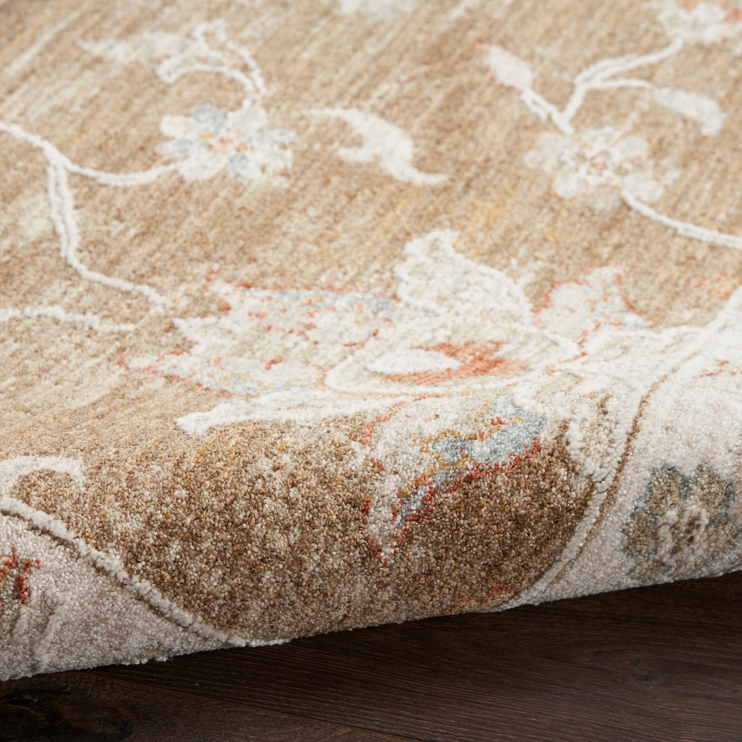 Beige floral patterned rug with cream, blue & peach accents; plush textured pile on dark wood floor.