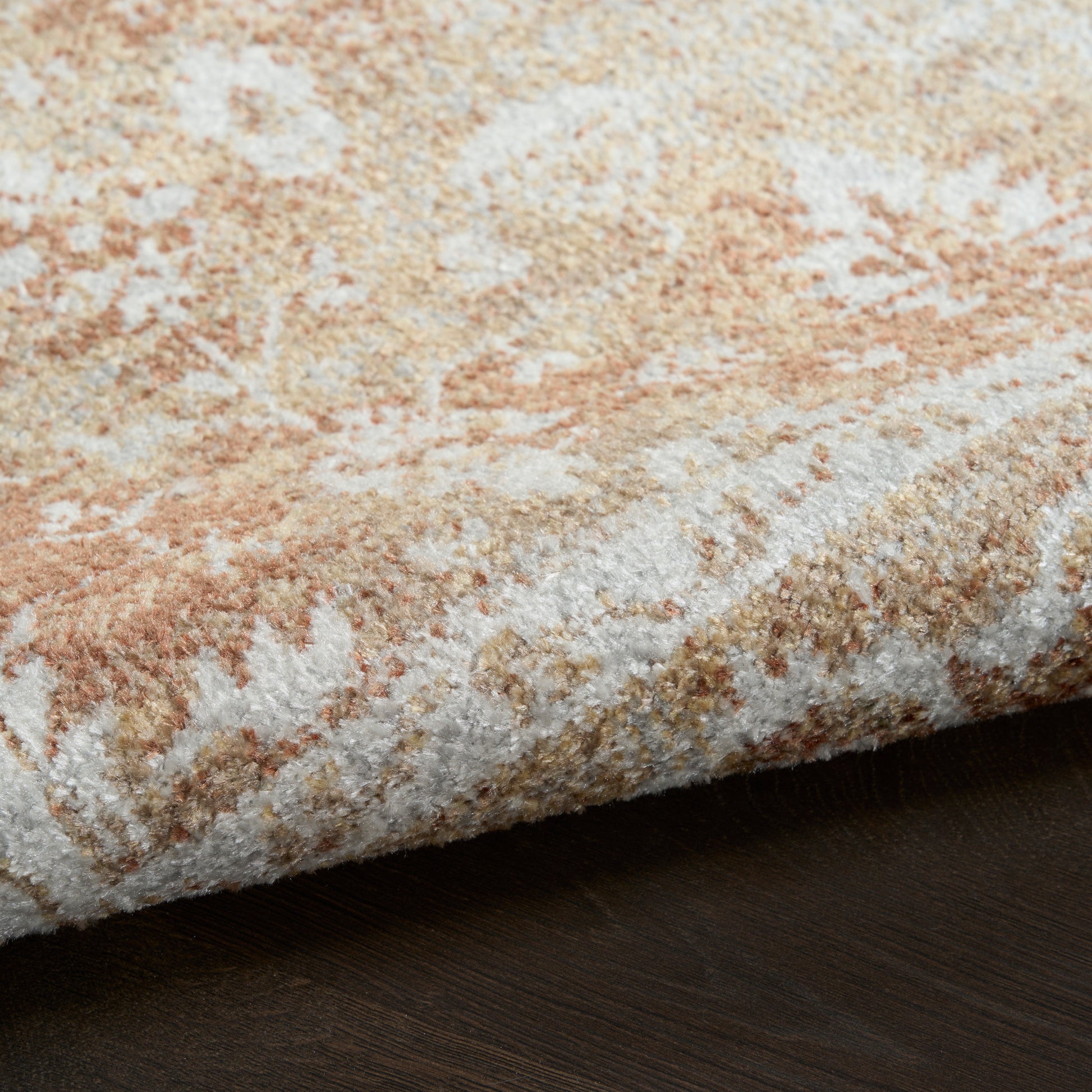 Close-up of a plush beige and cream area rug with taupe abstract pattern, edge folded on dark wood floor.