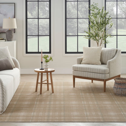 Bright living room with beige sofa and striped armchair, round wooden table, neutral rug, large black-framed windows, potted tree.