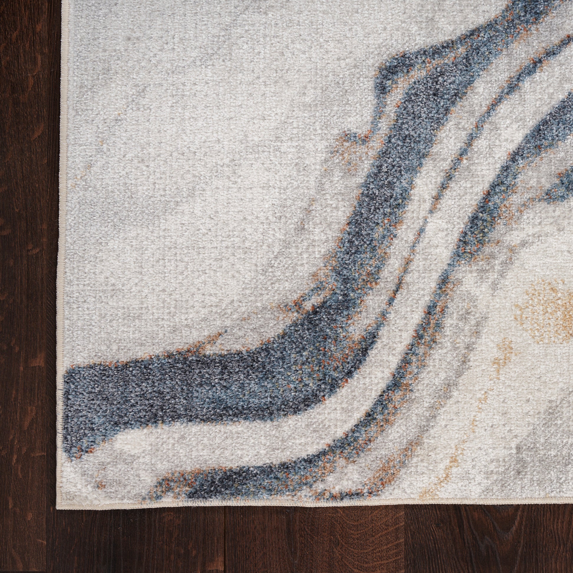 Abstract area rug with blue and gray wave stripes on ivory background, shown on dark wood floor.