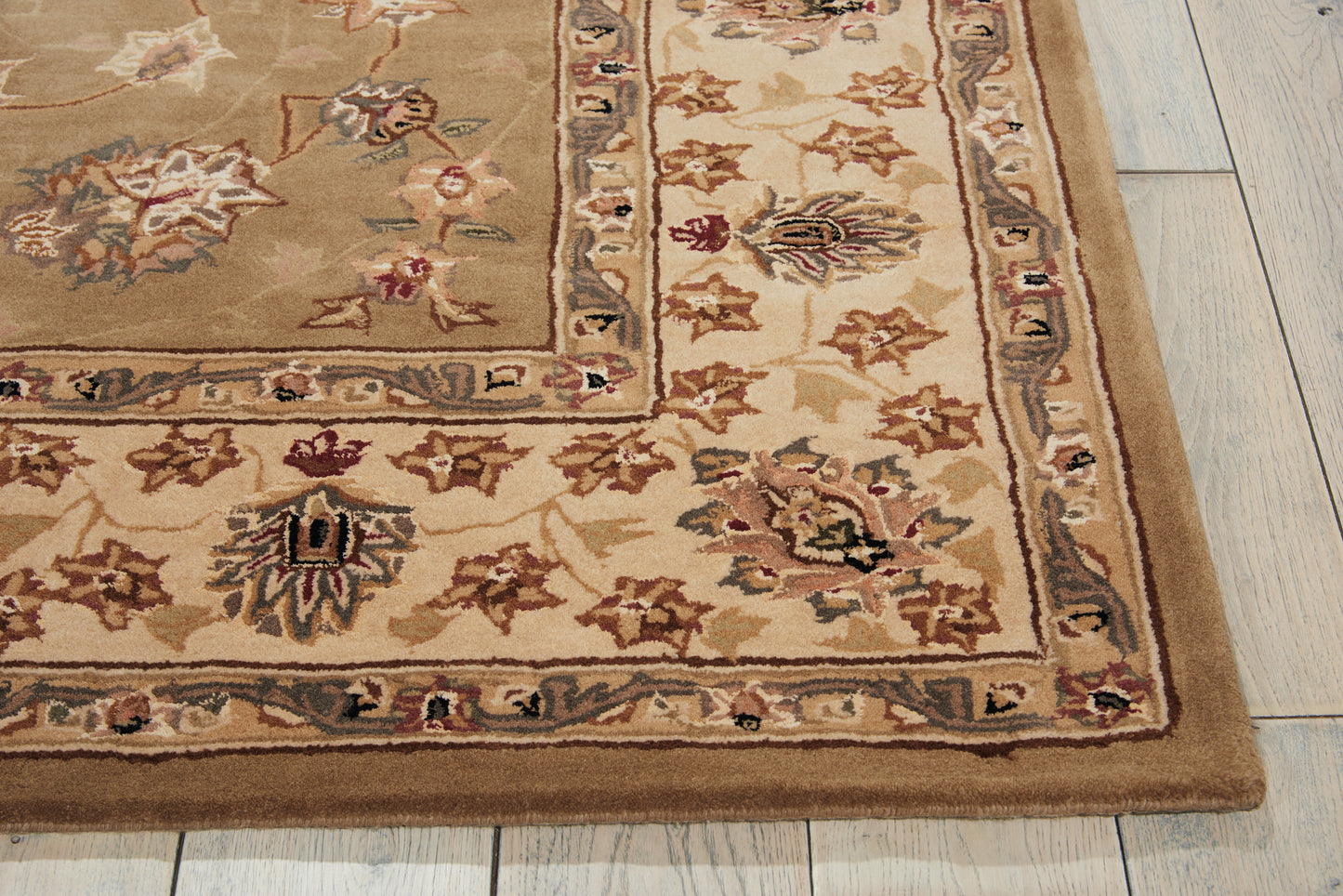 Beige oriental area rug with ornate floral border in browns, creams, and muted blues on light wooden floor.