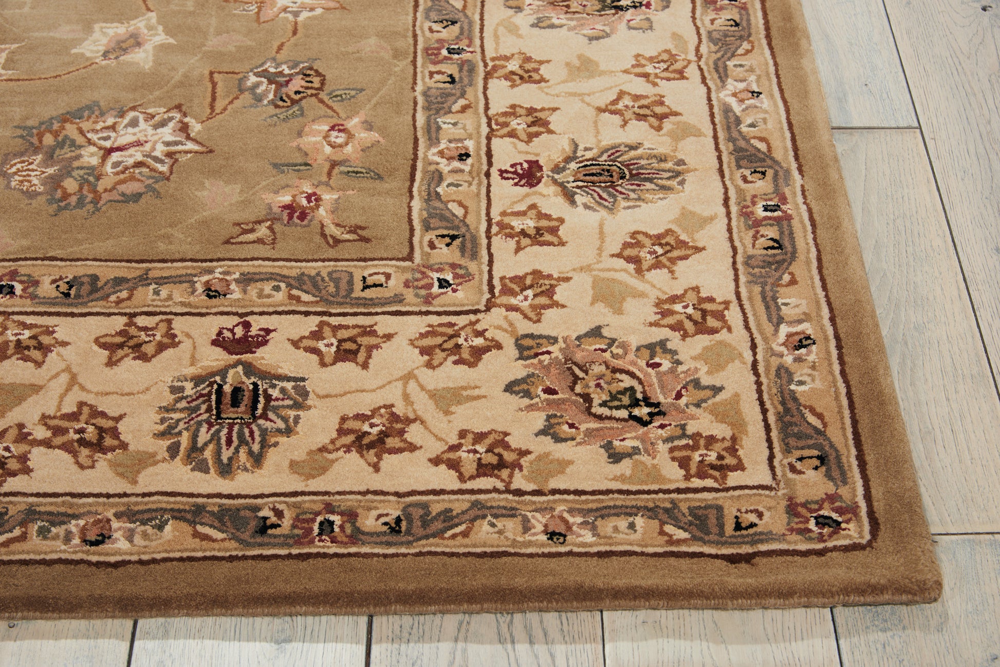 Beige oriental area rug with ornate floral border in browns, creams, and muted blues on light wooden floor.