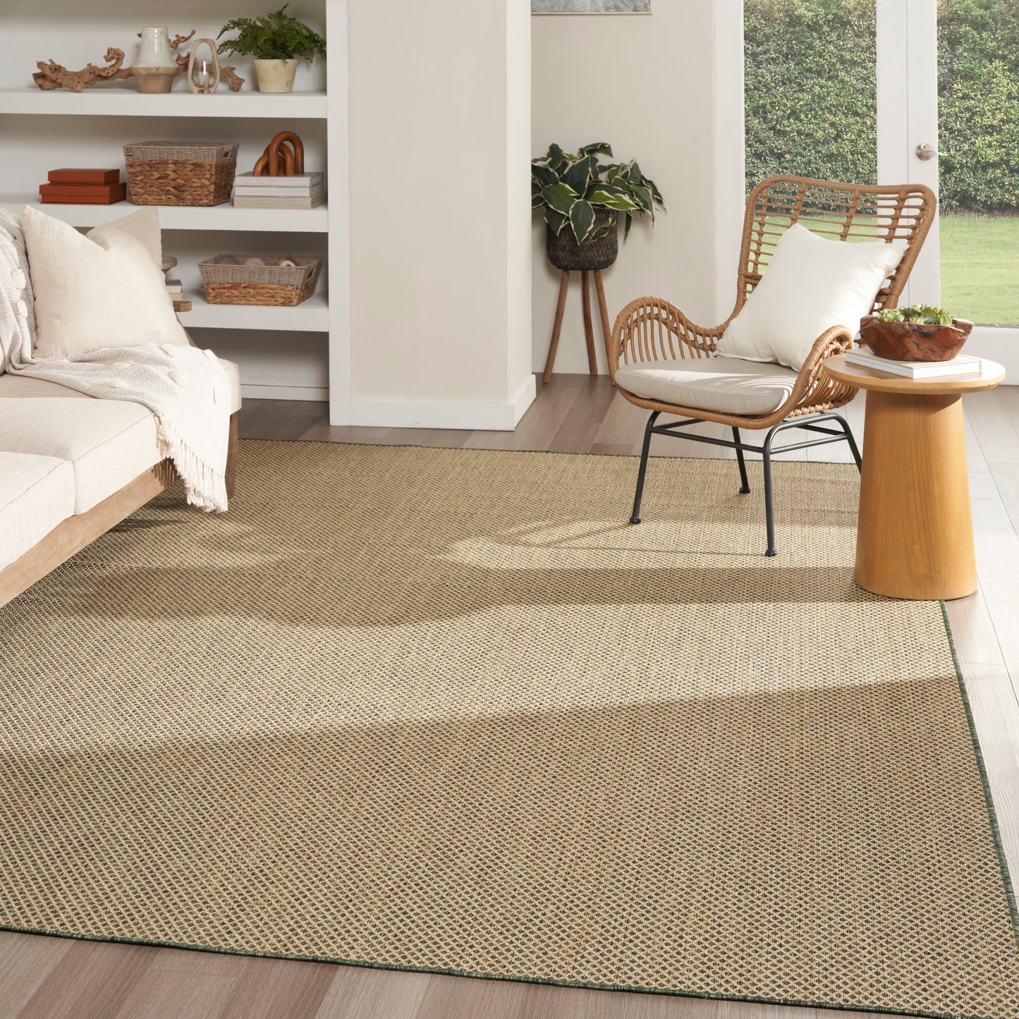 Bright neutral living room with a large woven jute rug, cream sofa, rattan chair, round wood side table, plants.