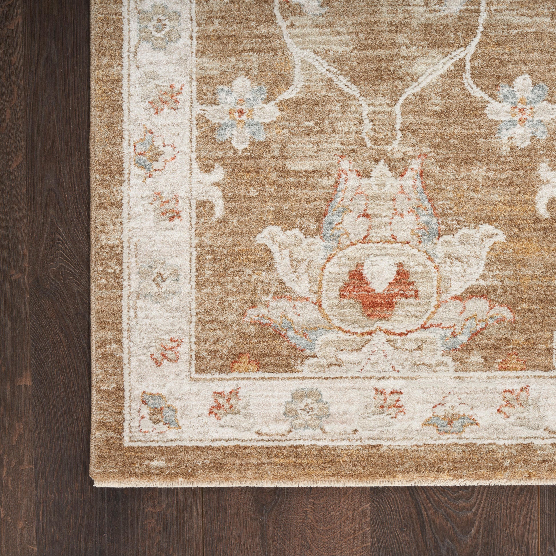 Ornate vintage-style rug corner on dark wood floor; brown field with ivory border and pale blue and pink floral motifs.