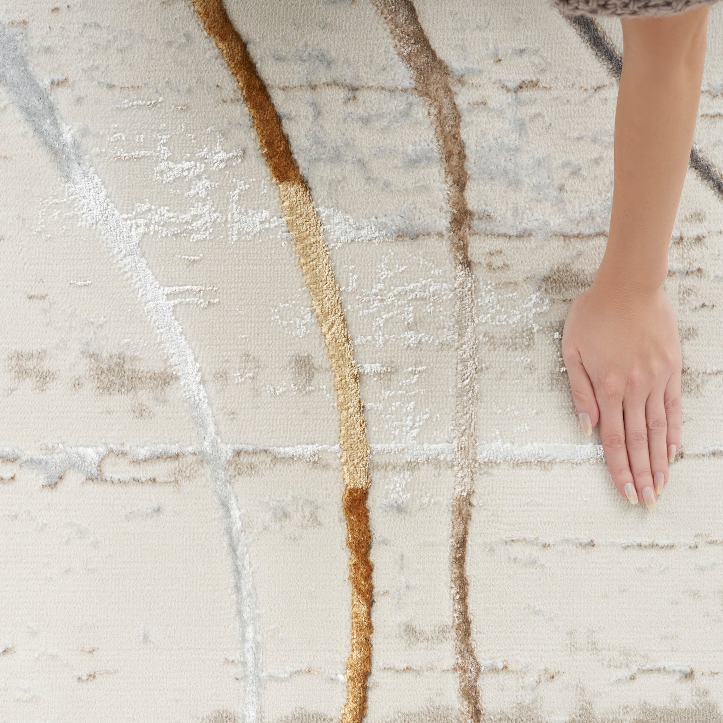 Beige woven rug with abstract curved tan, brown, and gray lines; hand resting on its surface.