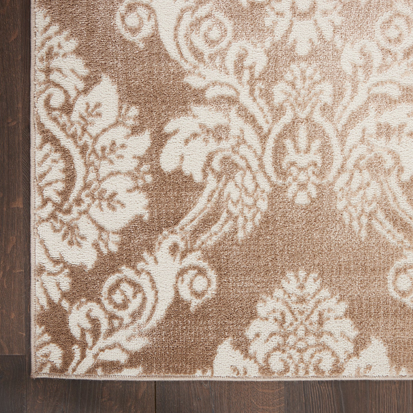 Rectangular brown and cream damask rug with ornate floral motifs; woven texture on dark wood floor.