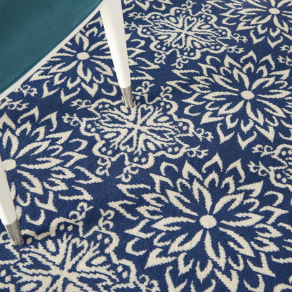 Navy blue area rug with white floral medallion pattern; soft woven pile under a glass-topped table with white legs.