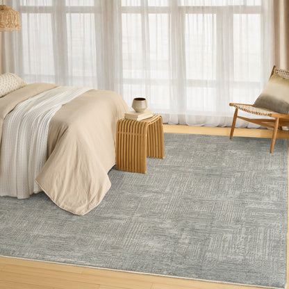 Neutral bedroom with beige bedding, light gray rug, wooden nightstand, ceramic cup, and woven lounge chair by sheer curtains.