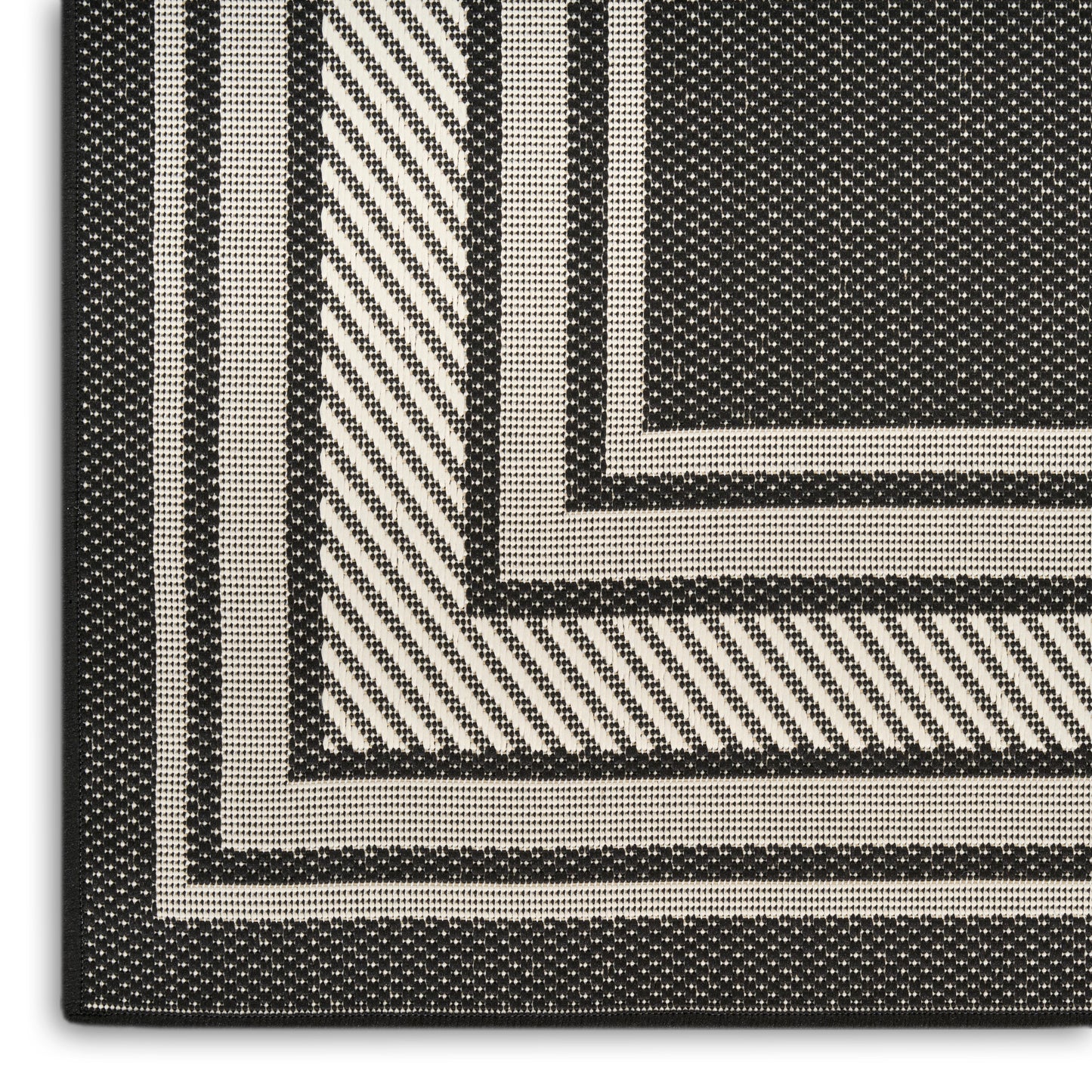 Close-up of black and ivory woven rug corner with concentric rectangular borders and diagonal stripe pattern.