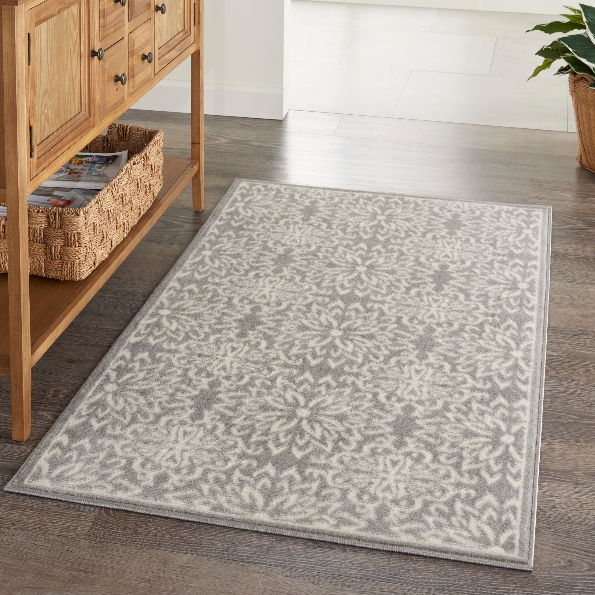 Rectangular grey and ivory damask-pattern area rug on dark wood floor beside a wooden console with a woven basket.