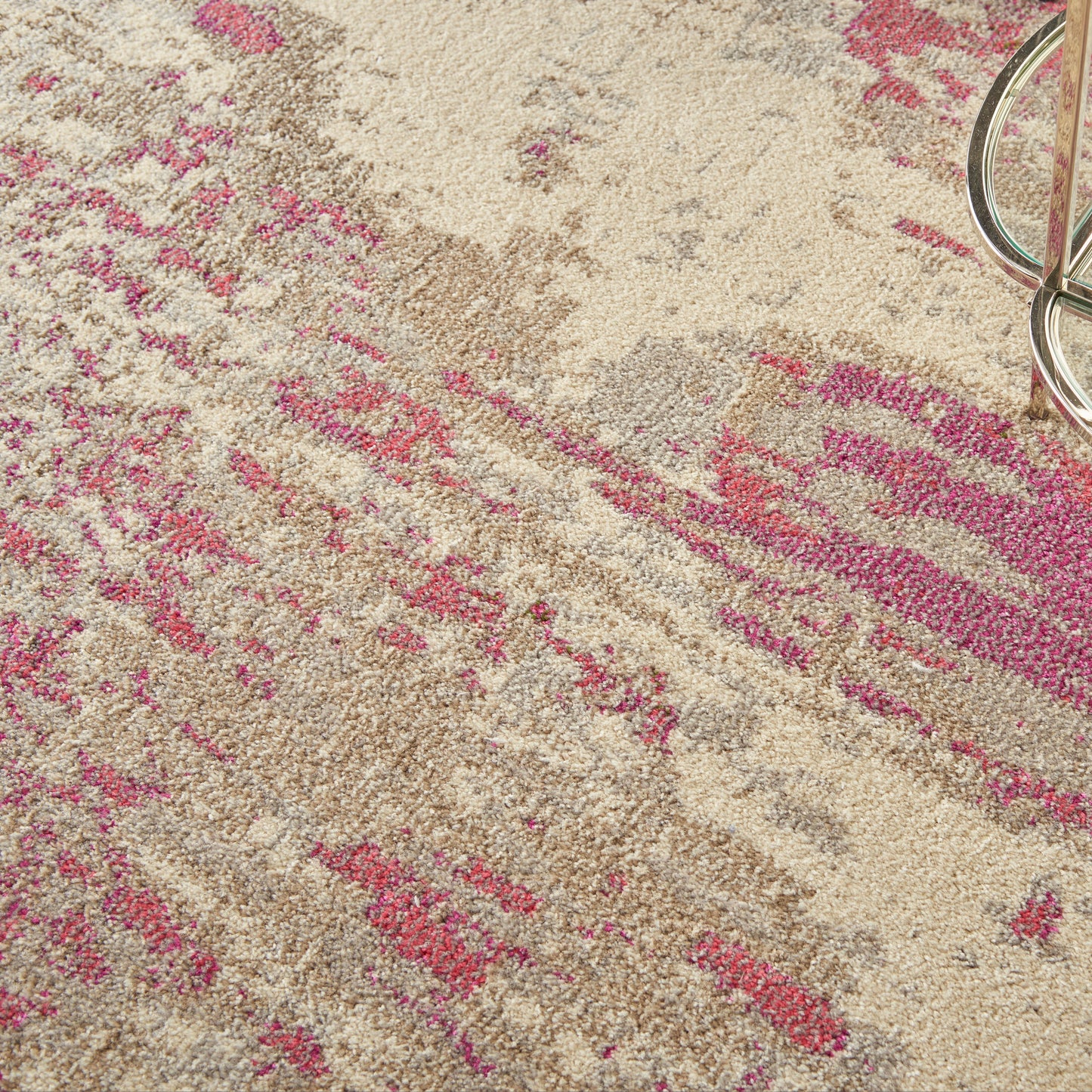 Beige area rug with pink abstract pattern and plush texture; metal circular ring in the top-right corner.