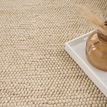Beige woven rug with a white tray holding an amber glass vase and dried pampas grass.