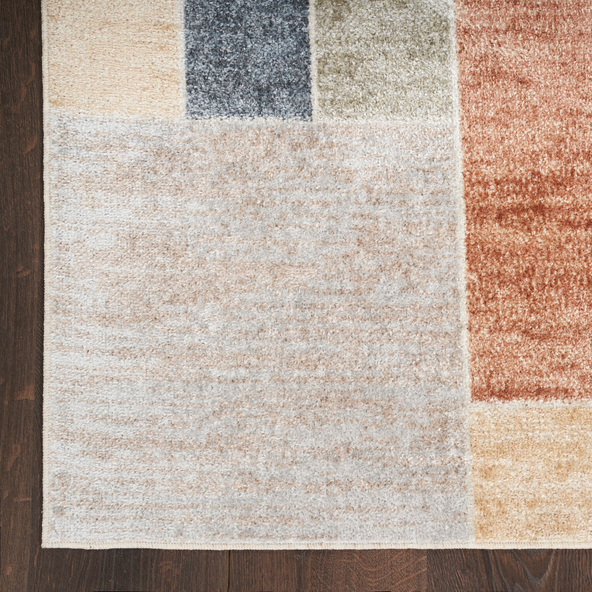 Patchwork area rug with beige, cream, blue, olive, rust & tan blocks on wood floor; soft texture, rectangular layout.