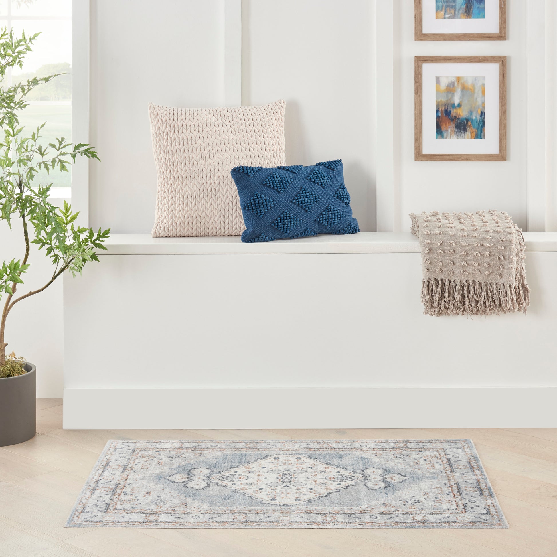 Beige knitted cushion, blue textured diamond pillow, beige fringed throw on white bench, blue-gray rug