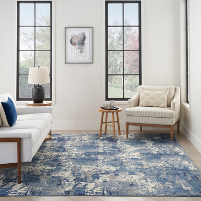 Bright living room with white sofa, beige armchair, blue abstract rug, black lamp, wood tables & large paned windows