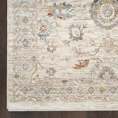 Ivory woven area rug with muted blue, gold & taupe floral medallions and ornate border on dark wood floor.