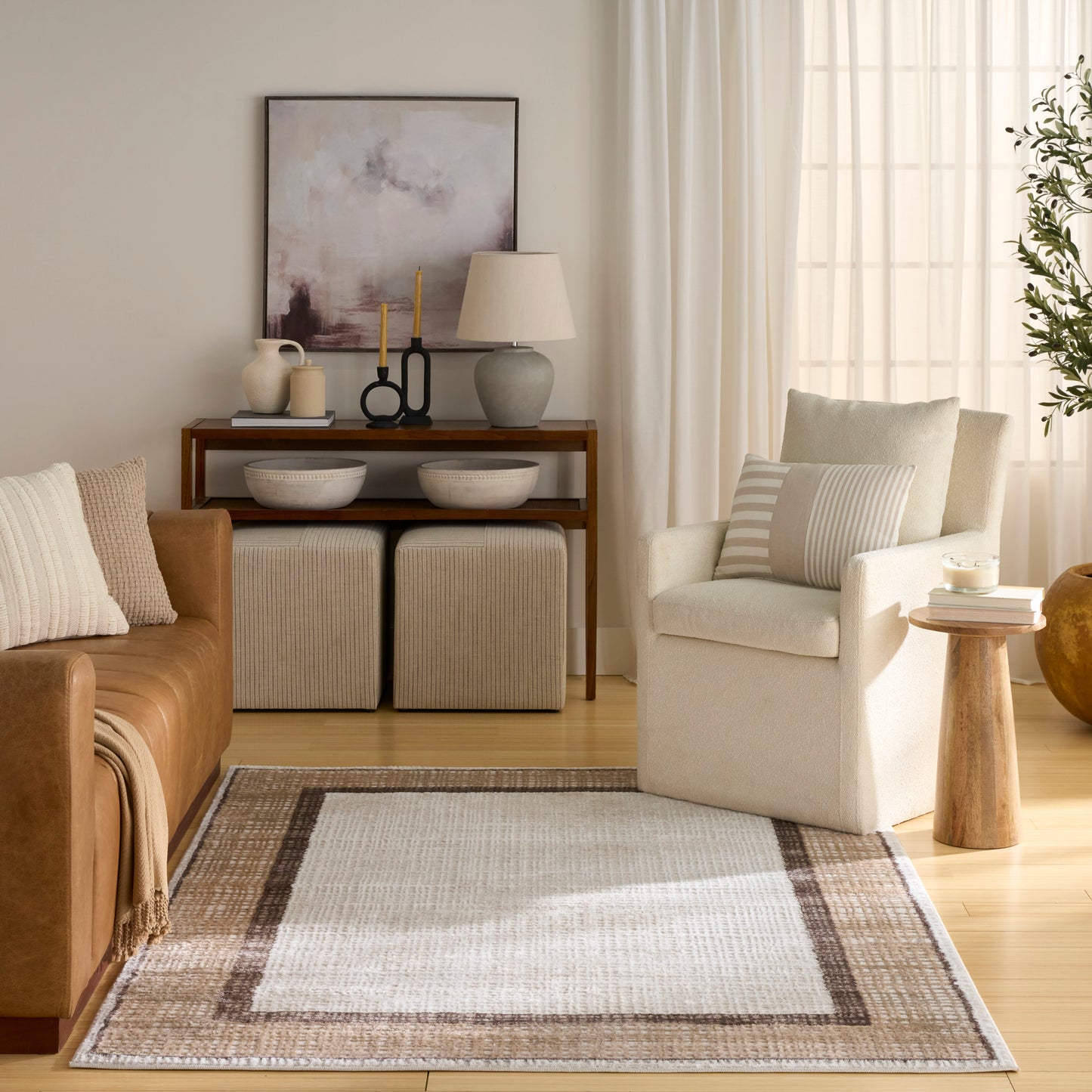 Neutral living room with tan leather sofa, cream armchair, striped pillow, woven rug, wooden console, beige ottomans.