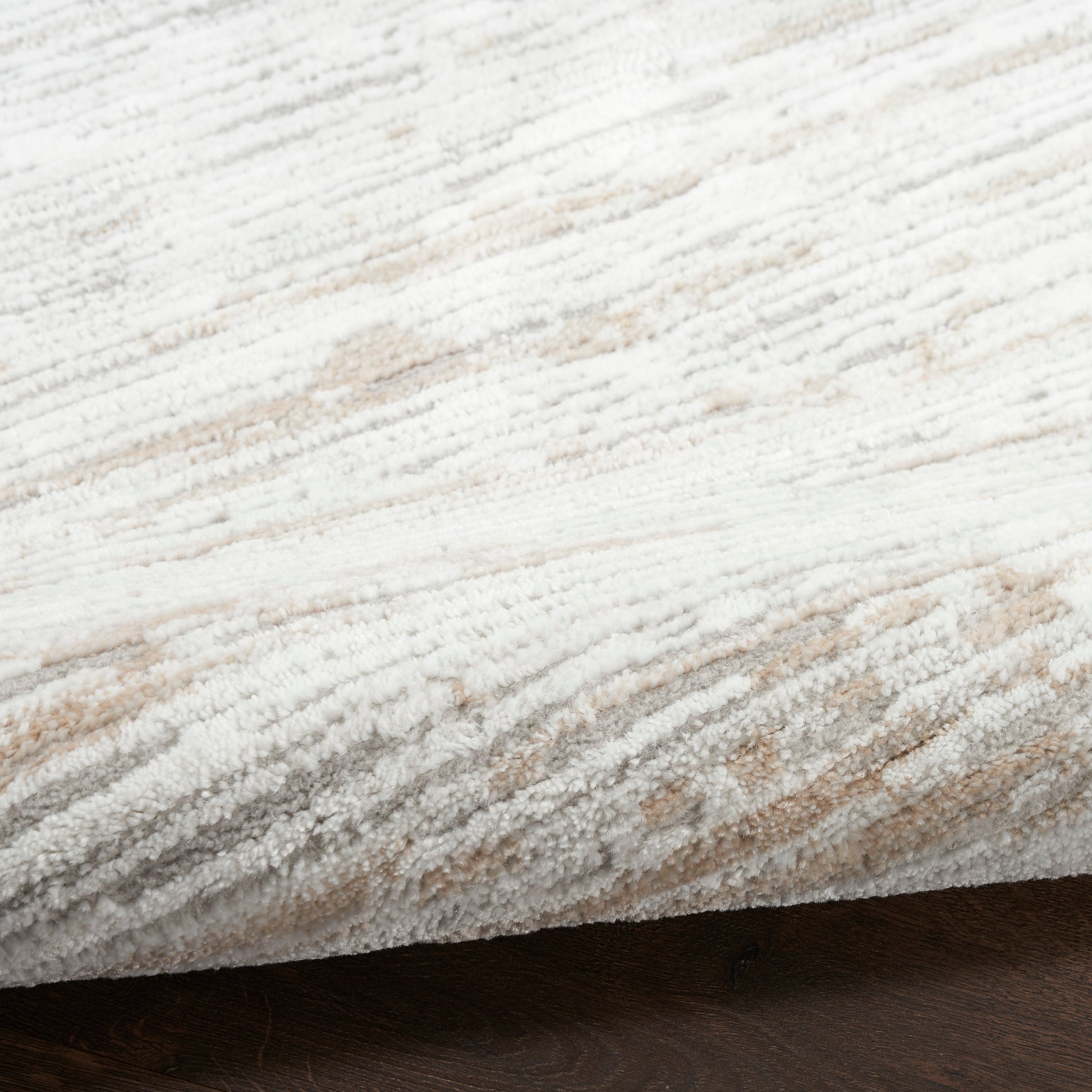 Close-up of plush cream and beige textured rug with subtle stripes on dark wood floor.