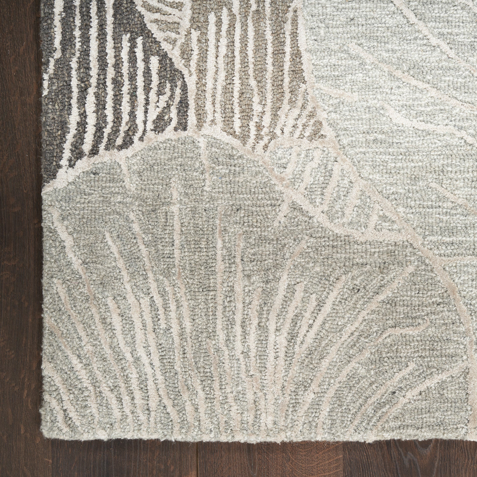 Neutral gray-beige area rug with abstract leaf pattern in textured pile on dark wood floor.