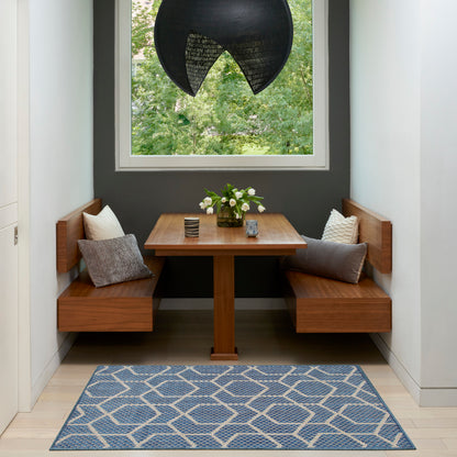 Wooden corner dining nook with square table, twin benches, gray wall, blue geometric rug, black pendant lamp, white flowers.