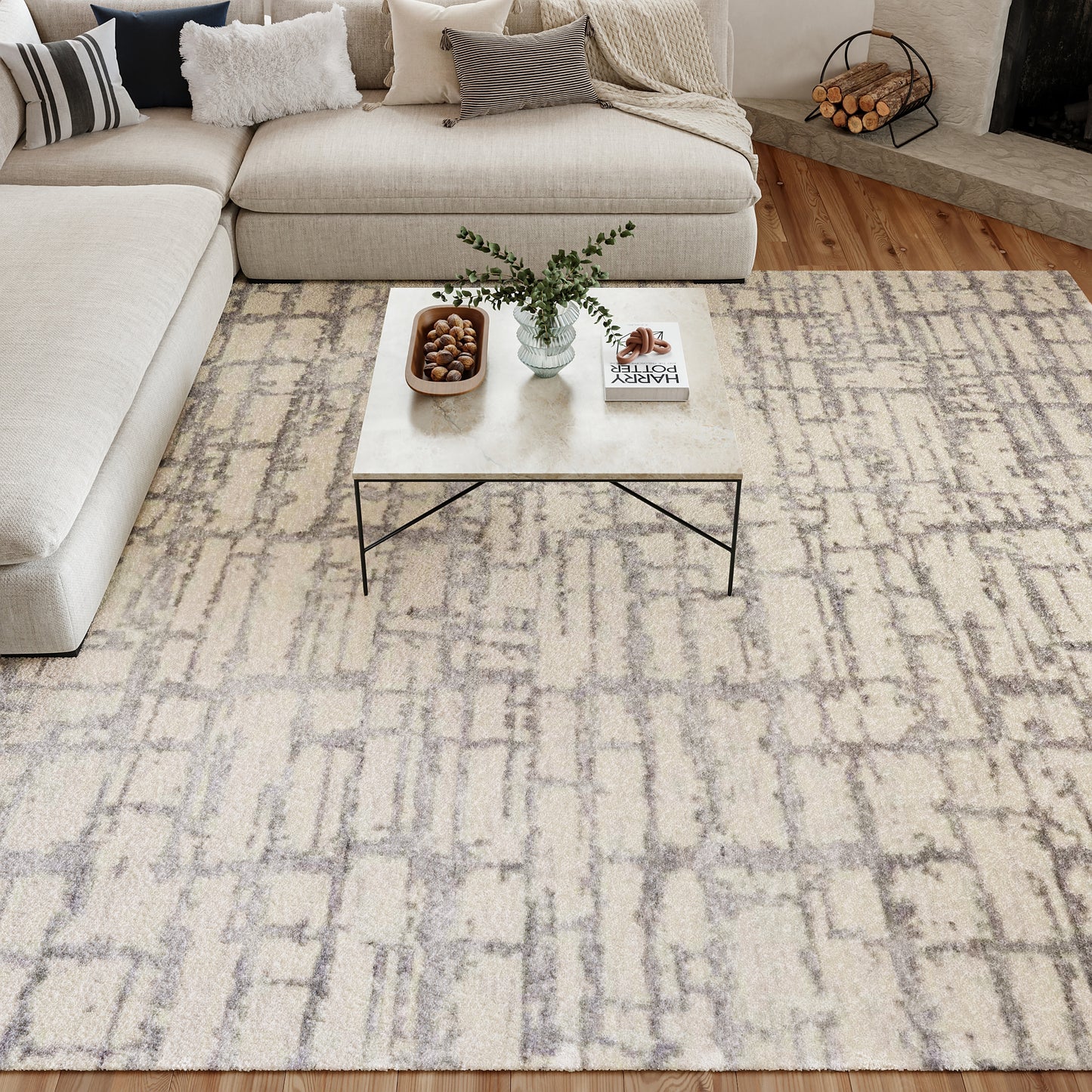 Beige sectional sofa with mixed cushions, cream abstract rug, square marble coffee table with black legs, vase of greenery.