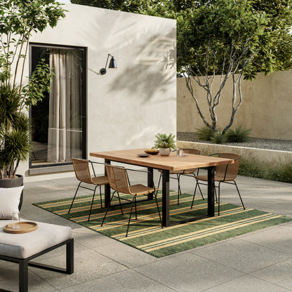 Outdoor rug: green striped 5' x 7' rug beneath a wooden table with black legs and wicker chairs against a beige stucco wall.