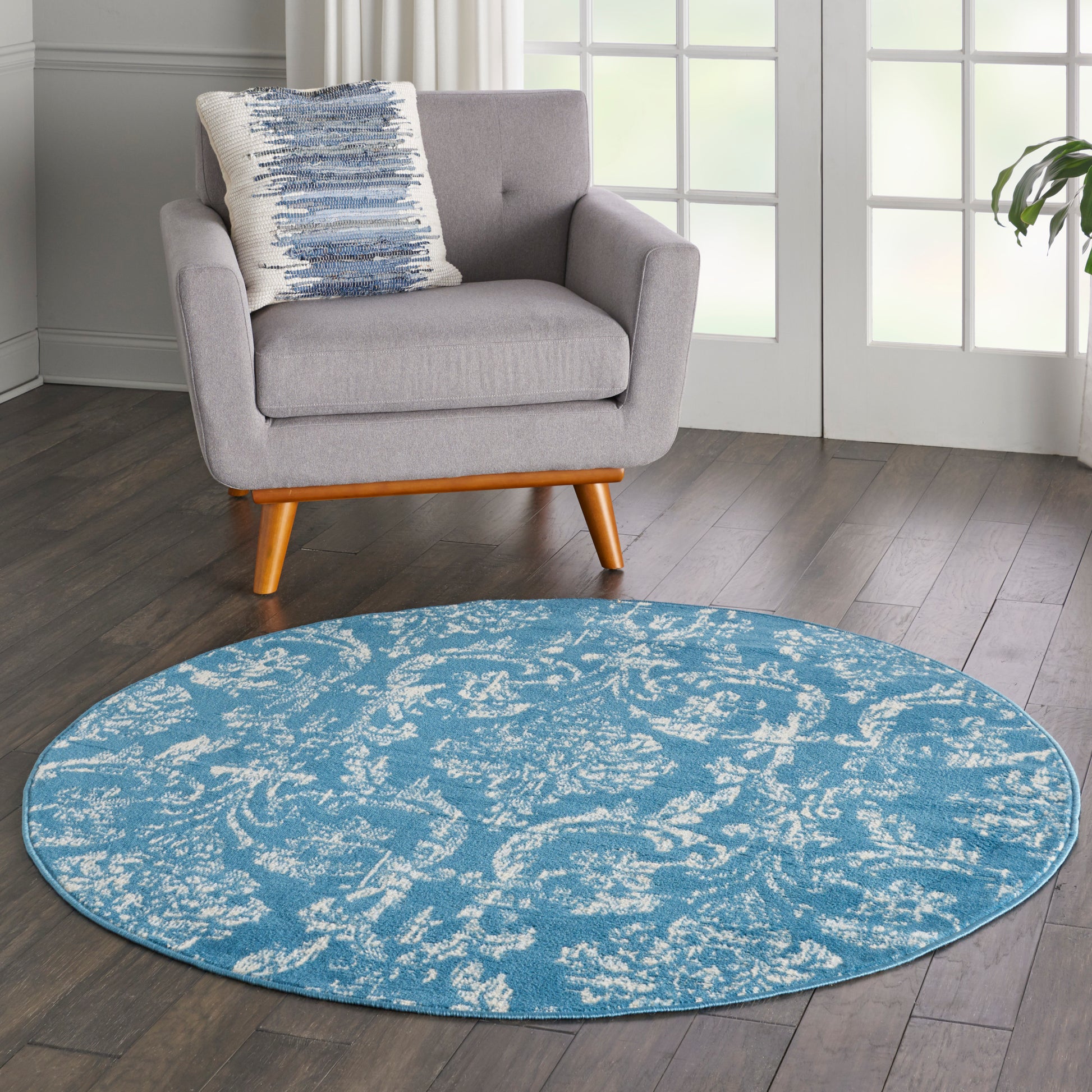Grey fabric upholstered mid-century armchair with wooden legs beside a blue circular rug with white abstract pattern.