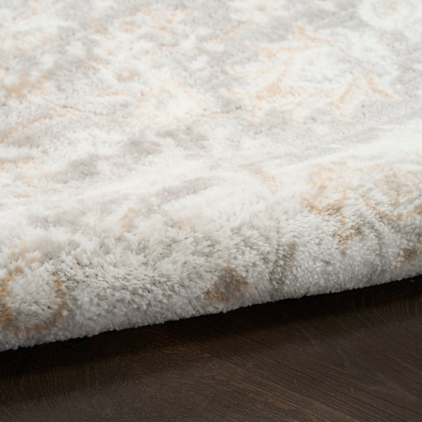 Soft white shag rug with beige accents and plush pile, folded edge on dark wood floor.
