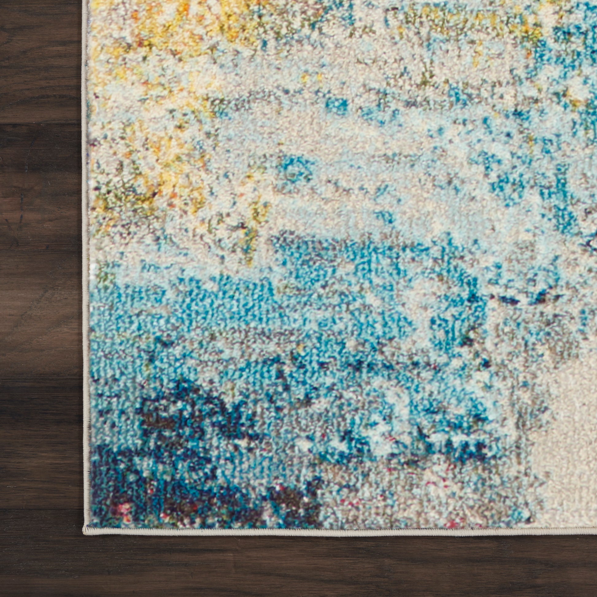 Rectangular abstract area rug with blue, teal, yellow and beige tones; distressed woven pattern on a wood floor.