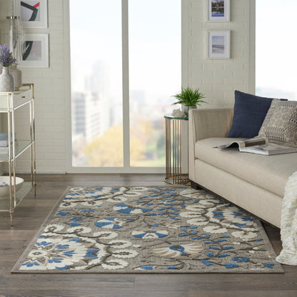 Rectangular beige-gray area rug with blue floral motif, set in a modern living room beside a beige sofa and large window.