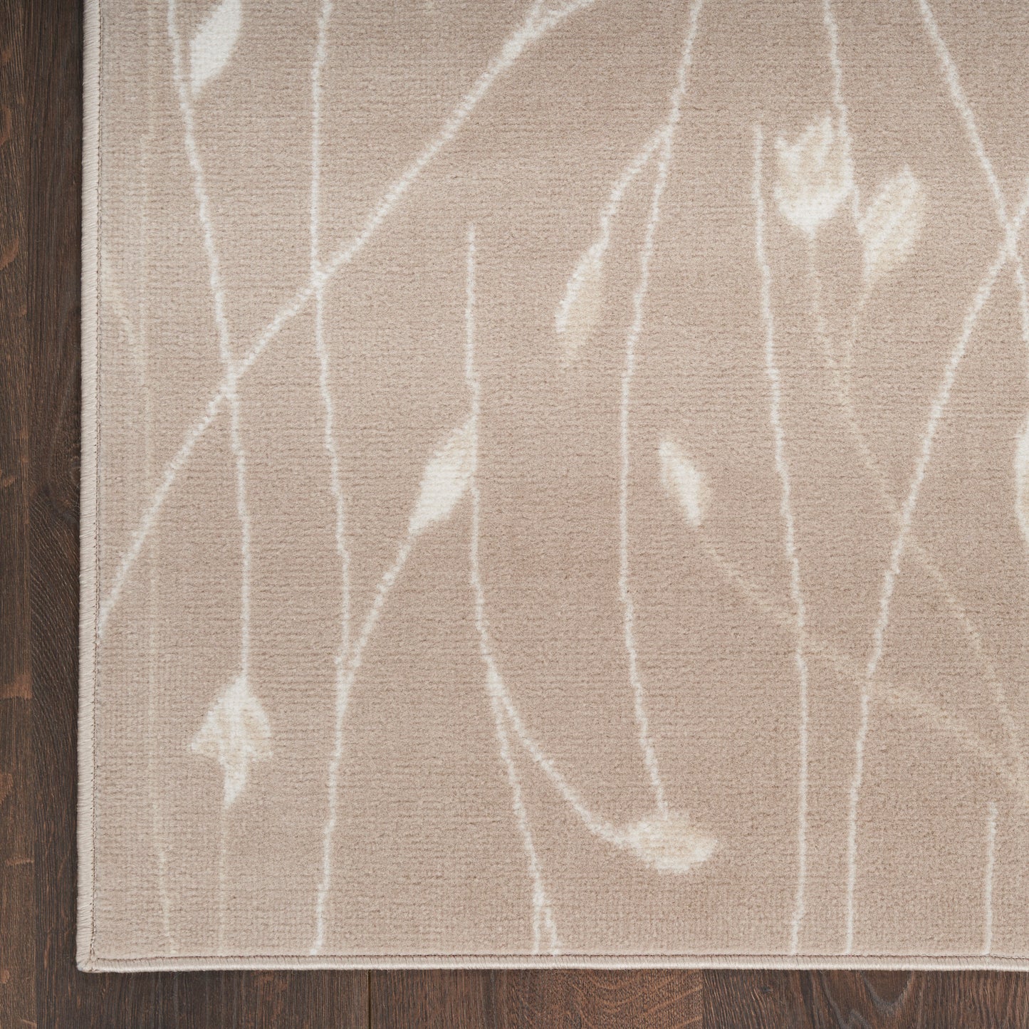 Beige rectangular area rug with white abstract vine pattern, soft texture, bordered edges, on dark wood floor.