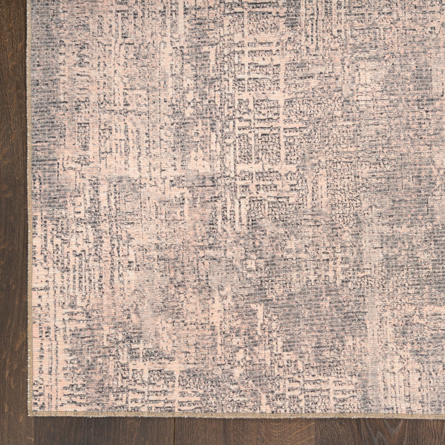 Abstract grey-blue rug with pink undertones on dark wood floor; distressed geometric pattern, rectangular.