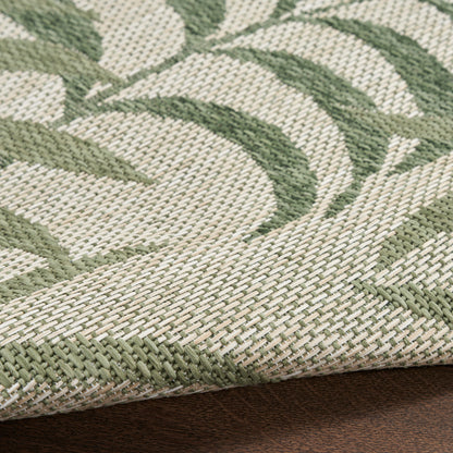Close-up of beige and sage-green woven rug with leafy pattern and rolled edge on dark wood surface.