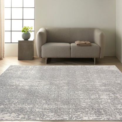 Light grey fabric sofa with rounded arms and metal legs, in front of a pale wall; blue-grey textured rug beneath.