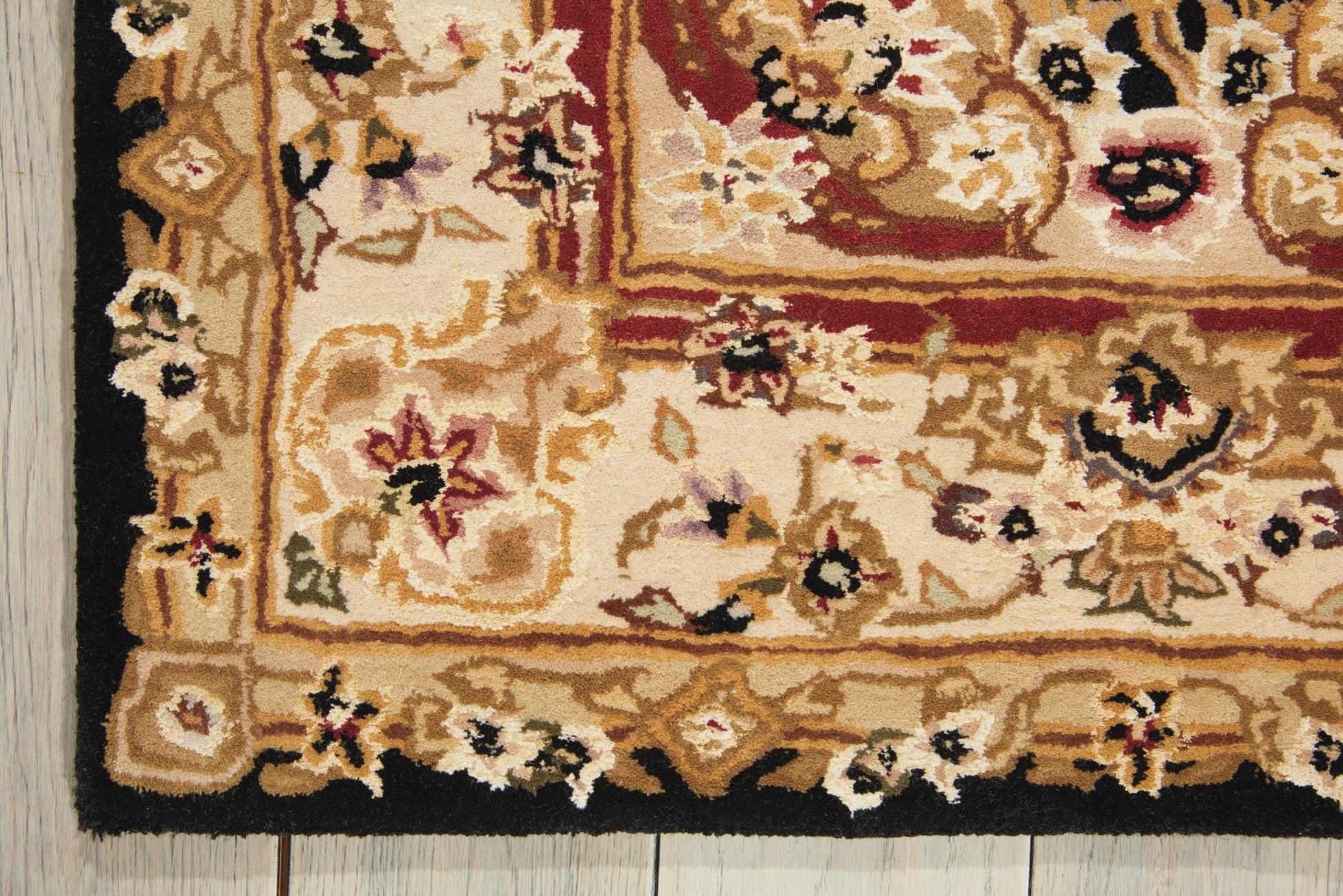 Traditional oriental rug corner with beige-gold field, pink/red floral motifs, black border on wooden floor.