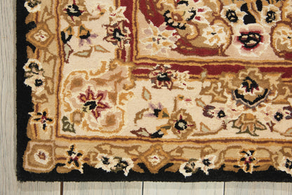 Traditional oriental rug corner with beige-gold field, pink/red floral motifs, black border on wooden floor.