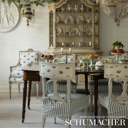 Shabby chic dining set: distressed white chairs with blue floral panels and striped seats, dark wood table, vintage cabinet.