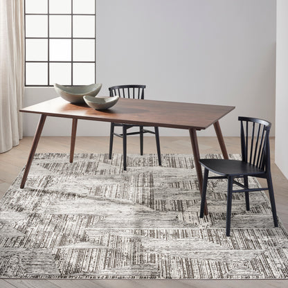 Rectangular walnut dining table with angled legs and black chairs; gray patterned rug and two green ceramic bowls on top.