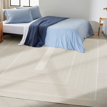Bedroom scene with a bed dressed in light to dark blue duvet, pale blue pillows, and a large beige geometric area rug.