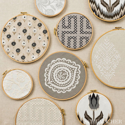 Assorted wooden embroidery hoops with beige, gray, and white fabrics featuring lace, geometric, and floral patterns.