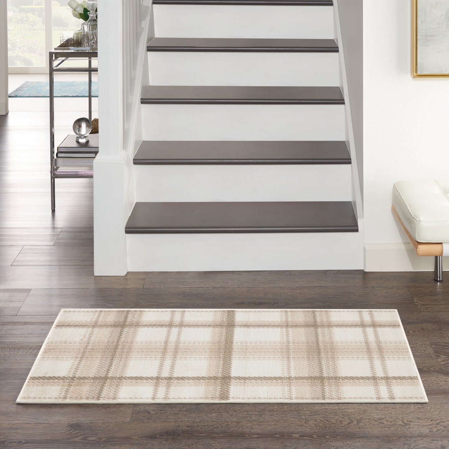 Beige plaid rug on dark hardwood floor, white staircase with dark treads, modern entryway with metal console.