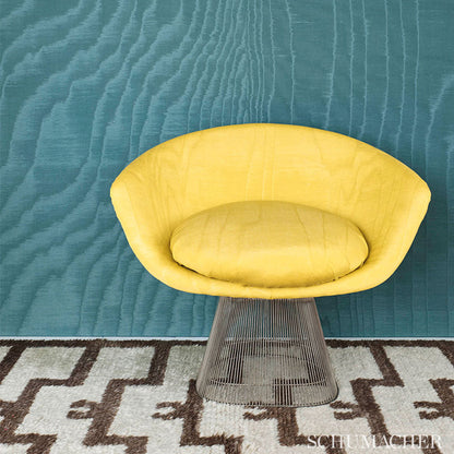 Bright yellow curved lounge chair with matching cushion on a metal wire pedestal base, teal textured wall and geometric rug.